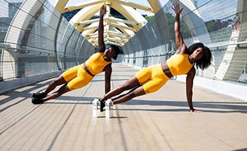 两名身穿黄色衣服的妇女在外面的一座桥上举起手臂做侧撑。