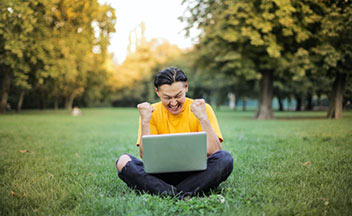 一个男人坐在草地上，膝上放着一台打开的笔记本电脑。