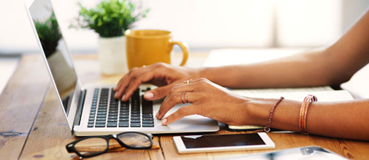 一个女人端着咖啡和手机在电脑上打字。